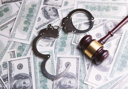 A gavel and handcuffs on top of one hundred dollar bills.