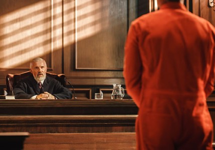 Offender in an orange jumpsuit giving testimony to a judge.