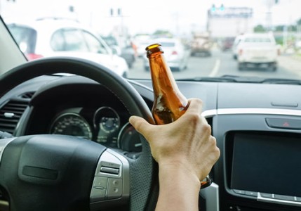 Driver holding alcoholic bottle while driving on busy road drunk driving.