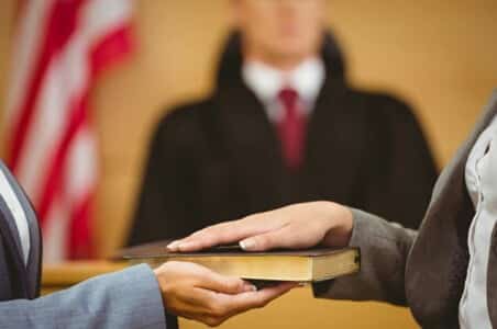 A witness with their hand on a bible taking the oath in court.