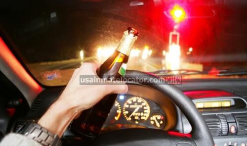 A man driving while drunk holding a beer bottle.