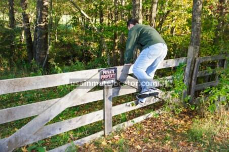 A man climbing over a fence with a no trespassing sign posted.