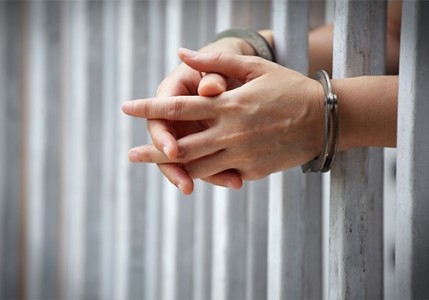 Handcuffed hands interlocked around prison bars.