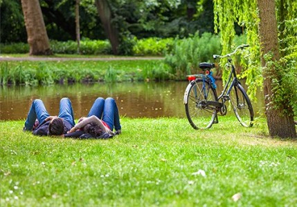 A young couple lying on their backs on the grass with a bicycle next to them.