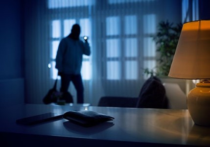 A burglar using a flashlight inside a house with a wallet in the foreground.