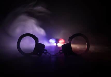 Silhouette of handcuffs against a background of smoke and police lights.
