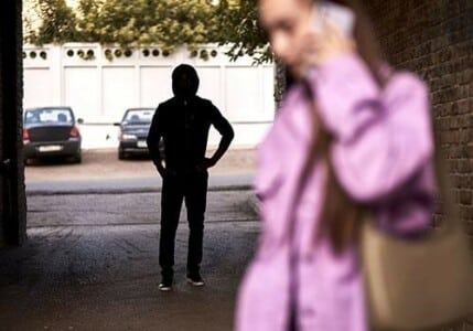 A woman on her cellphone with a stalker in the background.