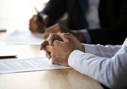 Clasped hands resting on documents on a desk.