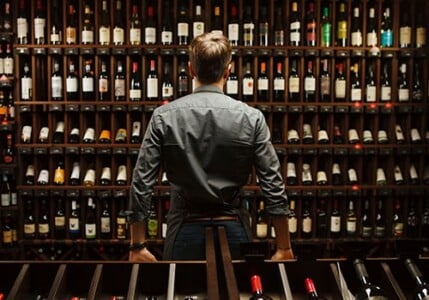 Worker looking at many bottles of wine on shelves.