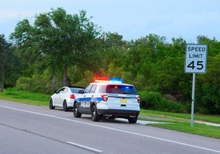 A police car with emergency lights on after stopping a car on the side of the road.