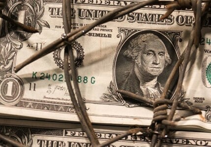 Dollar bills under rusty barbed wire.