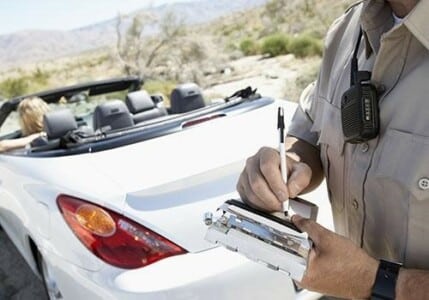 A police officer writing a speeding ticket to someone in a white convertible.