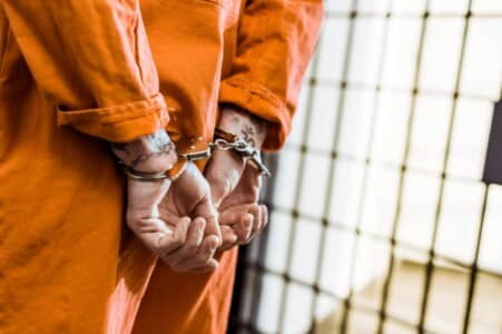 A prisoner in handcuffs wearing an orange jumpsuit.