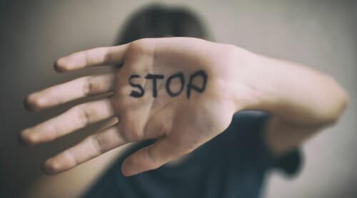 A woman with her hand up covering her face, with the word "STOP" written on it.