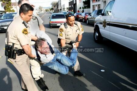 A man resisting arrest being carried by three police officers.